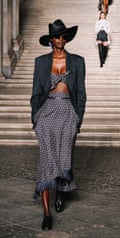 Model wearing matching long skirt and bra top with a black jacket and Stetson
