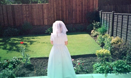 A woman dressed for a wedding in front of a perfectly mown lawn.