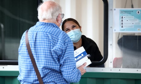 A smiling worker in a face mask gives an older man a box of free rapid antigen tests