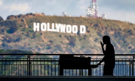 A worker wheels equipment past the famous Hollywood sign.