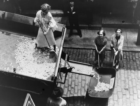 Women sweeping coins from a truck into a wheelbarrow
