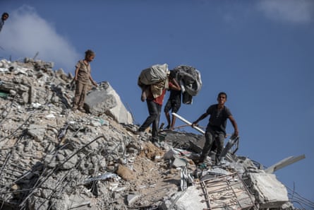 Men and children climb on top of concrete rubble and rebar, holding bags on their heads and shoulders.