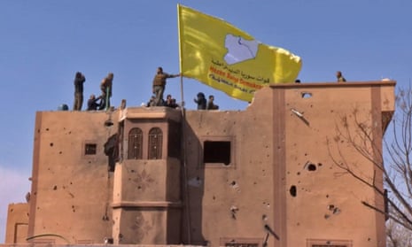 US-backed Syrian Democratic Forces (SDF) fighters raise their flag on a building in Baghuz.