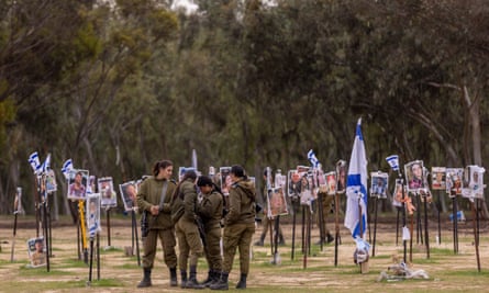 Israeli solders walking among a display of photos of people killed during the Hamas attack at the Nova festival site.