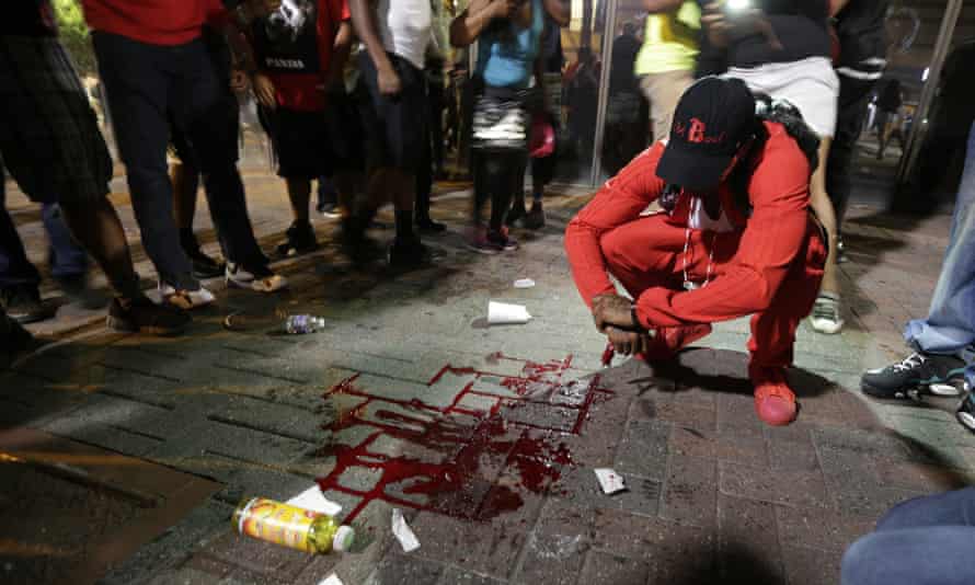 A man squats near a pool of blood after a man was injured during a protest of Tuesday’s fatal police shooting of Keith Lamont Scott in Charlotte.