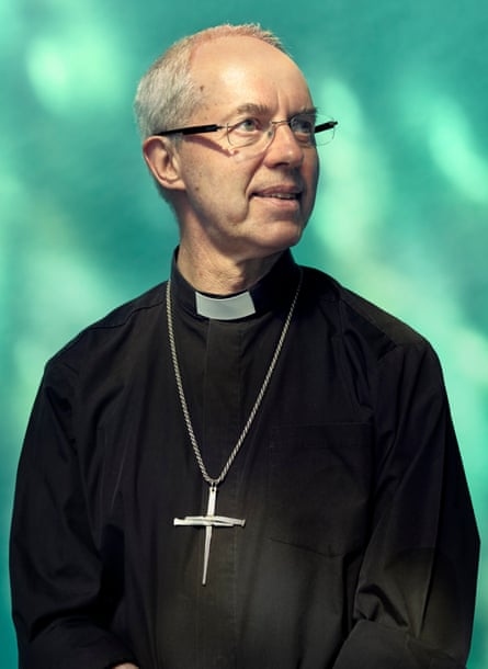 Justin Welby, con gafas y un gran crucifijo en una cadena, mira hacia arriba, sonriendo levemente.