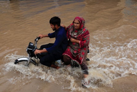 People ride a motorbike along a flooded road in Sialkot.