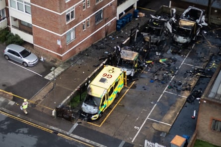 An aerial view of the scene of the fire showing the burned-out ambulances in a car park, with burnt debris around, and fire damage to a block of flats to one side.