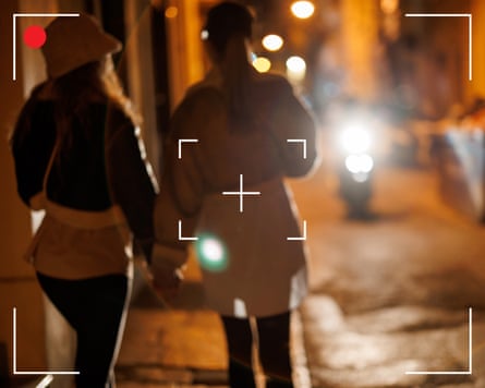 عرض خلفي لامرأتين تمسكان بأيدٍ وتتمشيان في المدينة ليلاً مع إطار منظر الكاميرا فوقه