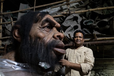 A man standing next to the large head of a cave man figure.