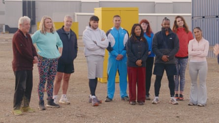 A crowd of contestants stand in front of a yellow shipping container.