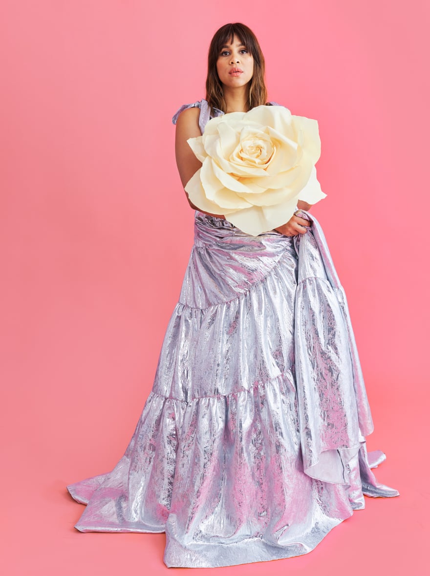 Zawe Ashton wearing a silver dress and holding a large hat in the shape of an open rose