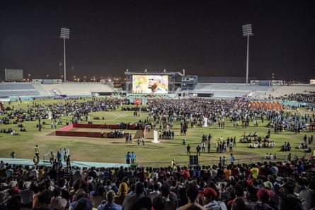 Darbuotojai migrantai žiūri į Katarą prieš Ekvadorą dideliame ekrane iš kriketo aikštės gerbėjų zonos Dohos pakraštyje.
