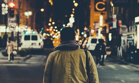 Rear View Of Man Walking On Illuminated Street Amid Buildings