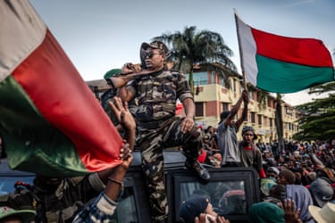 Protesters wave flags as members of the CAPSAT in military uniforms ride on an armoured vehicle