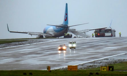 A plane on one side of a runway with emergency vehicles around it.