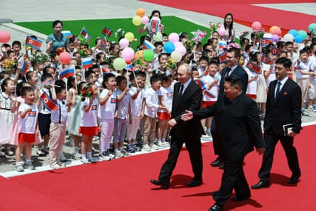 Kim Jong-un and Vladimir Putin walk along a red carpet flanked by spectators, many of them children holding flags and balloons