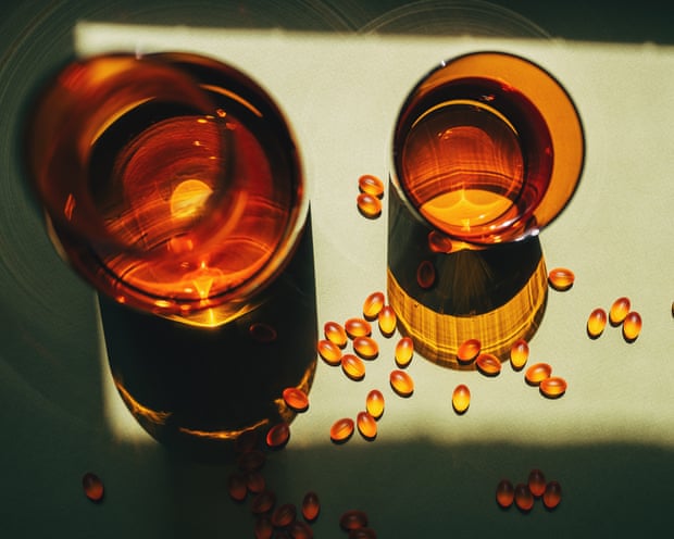 Overhead view of two amber glasses and scattered Omega-3 capsules on a green surface in sunlight