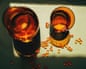 Overhead view of two amber glasses and scattered Omega-3 capsules on a green surface in sunlight