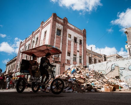 A pedicab cycles past a large pile of rubbish on a street corner