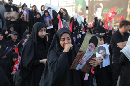 A woman cries holding a photograph of Ali Khamenei, surrounded by other attenders of the funeral.