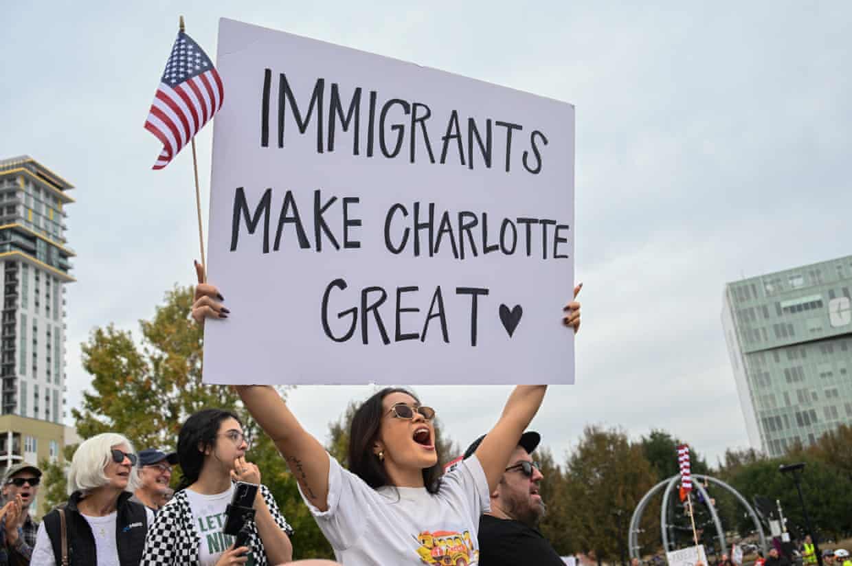 woman holds up small american flag and sign saying ‘immigrants make Charlotte great’ at protest outside
