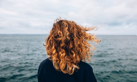 woman with red curly hair looks out to sea