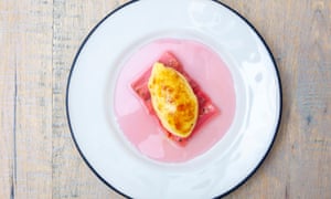 A round white plate with an oblong of rhubarb pieces and an oval of custard on top, and pink juice on the plate