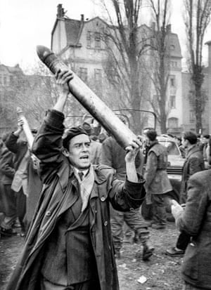 Un luchador tiene triunfalmente un proyectil de un tanque soviético saqueado, que llegó en un camión para ser utilizado en tanques rebeldes con banderas húngaras