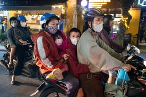 Two children sit between two adults on a moped all wearing facemasks and the adults wear helmets.