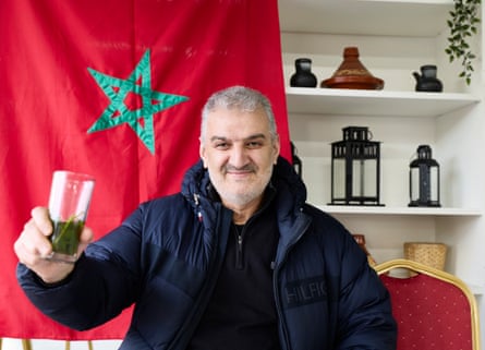 Moroccan Mohamed Chelh holds up a glass of mint tea, with a Moroccan flag in the background.