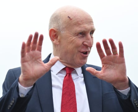 John Healey wearing a suit and tie and holding up his hands