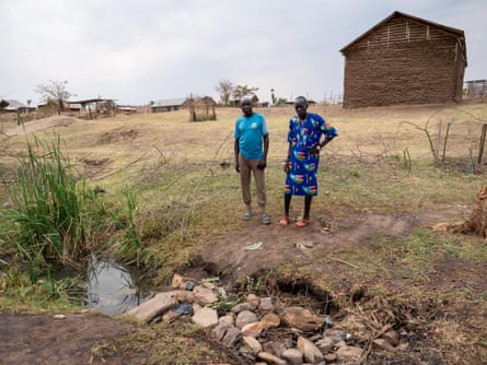 Two people stand looking at a small pool of water in a patch of muddy ground