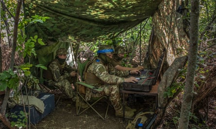 Ukrainian drone operators working hidden in a shady copse near the frontline. A screen in front of them offers a panoramic view of the war.