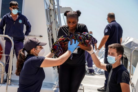 Two people help a woman holding a baby off a ship
