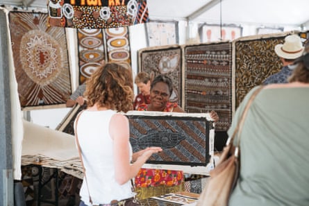 Indigenous artist showing artwork to market patron.