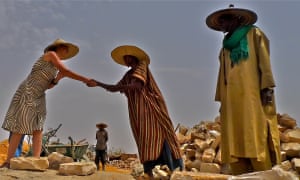 A lady shakes hands with a local man while another looks on. All three wear wide hats.