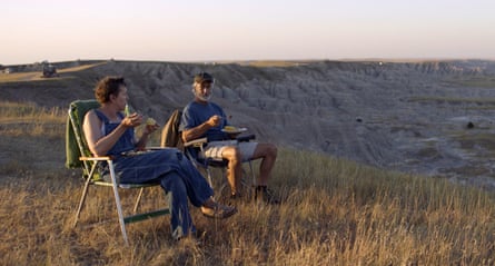 A woman and a man sit on lawn chairs at dawn on a grassy hill.