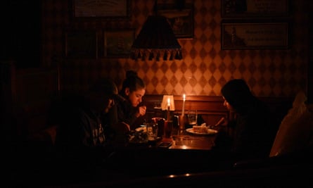 Candles illuminate the faces of two people eating lunch in a darkened room