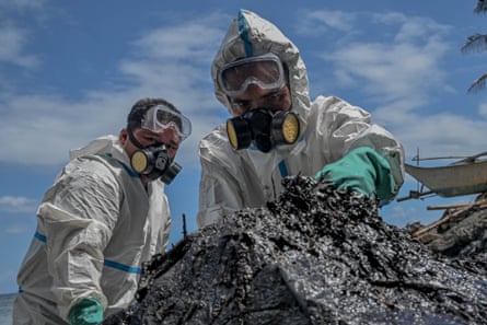 Two people in white overalls, goggles and gas masks pile up contaminated sand