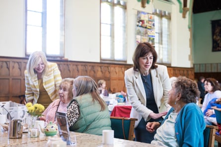 Two women, who are standing up, talk to women sitting down at a cafe