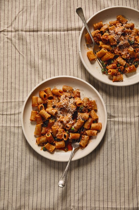 Mezzi rigatoni with pork ragù & peas, served in two white bowls sitting on a striped tablecloth