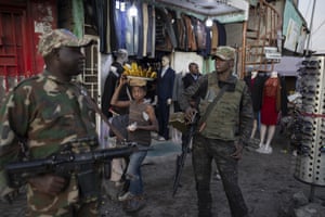 A girl selling bananas hurries along as soldiers patrol the streets in Goma