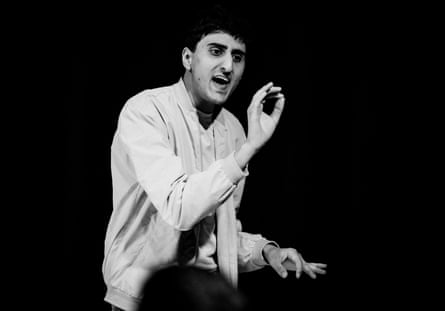 Mehrabani sitting on stage in a white jacket and black trousers against a white background.