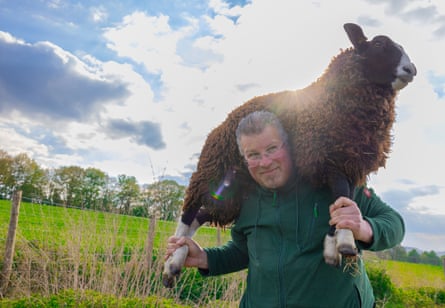A man holds a brown sheep on his shoulders