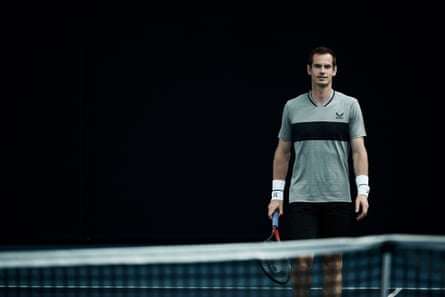 Andy Murray stands behind a tennis net wearing a grey top with a wide black stripe and AMC branding with Castore’s birds-wing logo.