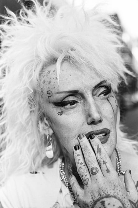 A punk woman with spiky blond hair, strong makeup and tattoos on her hand and face