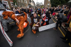 Pantomime horses run in the street as organisers try to block their path with jumps.