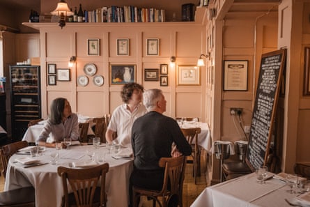 Diners sit at a table in Bouchon Racine and look at a blackboard with a menu chalked on it.