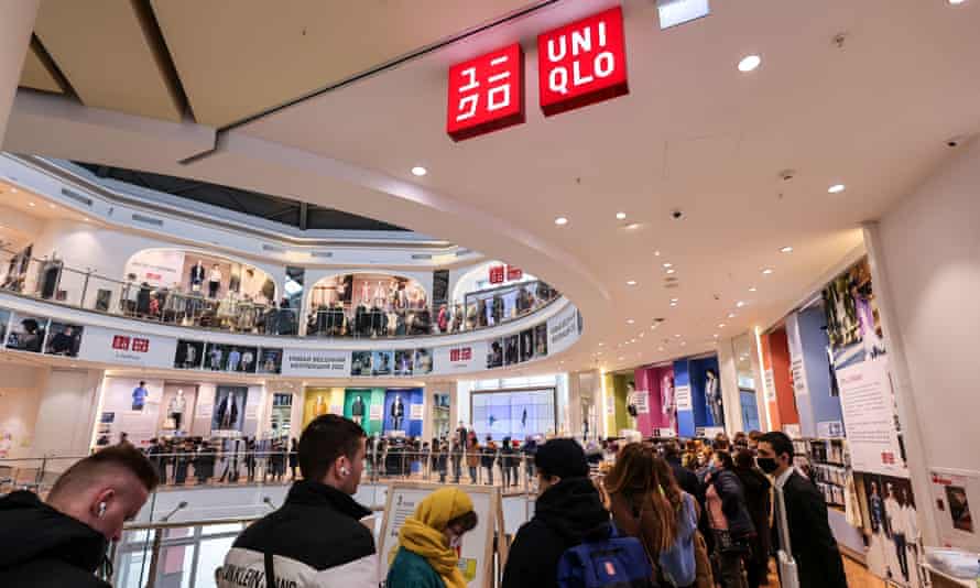 View inside a shopping mall of a long queue winding up spiral stairs, with a red Uniqlo sign hanging from the ceiling above the people